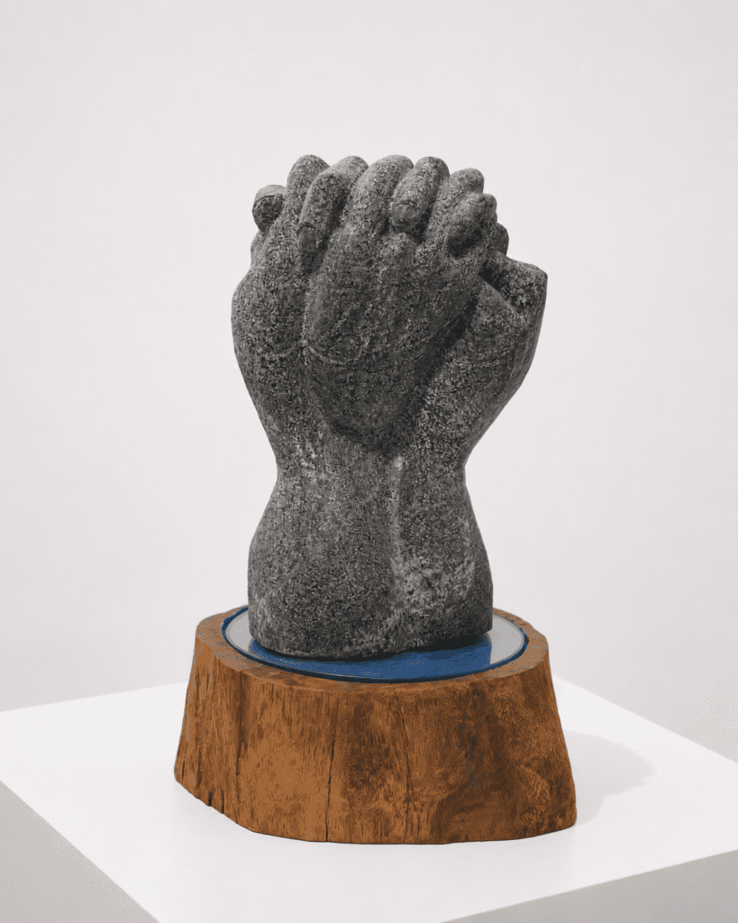 Handcrafted granite sculpture featuring interlocked hands symbolizing strength, togetherness, trust, and human connection. Displayed on a natural wood pedestal, this contemporary artwork blends organic materials and sculptural artistry, making it a meaningful statement piece for galleries, luxury interiors, architects, and art collectors.