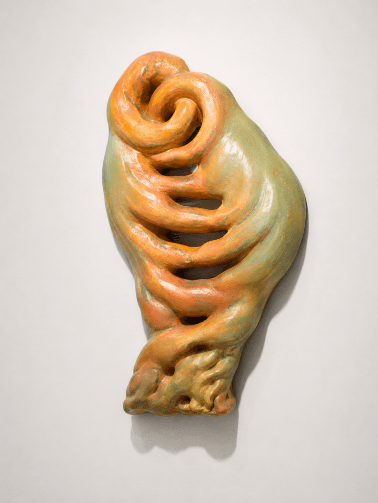 Modern abstract wall sculpture with intertwined spiral shapes and organic contours in earthy orange and green hues. A contemporary artistic piece inspired by nature, movement, and the evolution of form, created by sculptor V K Rajan.