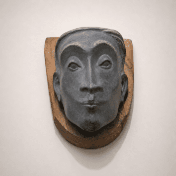 Abstract stone face wall sculpture with wooden base, handcrafted by sculptor Johns Mathew. A contemporary art piece showcasing expressive facial features, natural textures, and minimalist gallery aesthetics.